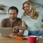 German Mietmakler (rental agent) shaking hands with young couple in front of apartment with Zu Vermieten sign